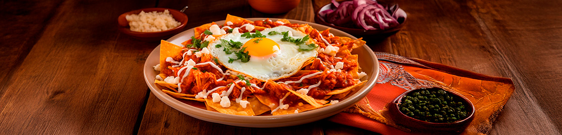 foto de un plato de chilaquiles rojos horneados con un huevo frito encima sobre una mesa de madera.