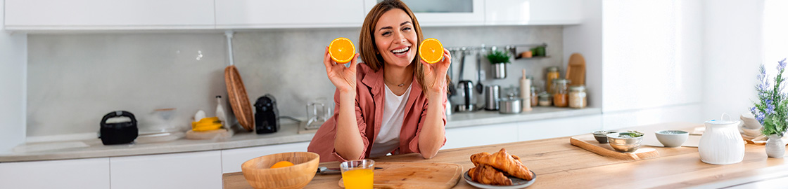 foto de mujer apoyada en la barra de la cocina con naranjas y jugo de naranja, fruta que ayuda a mantener las defensas altas.