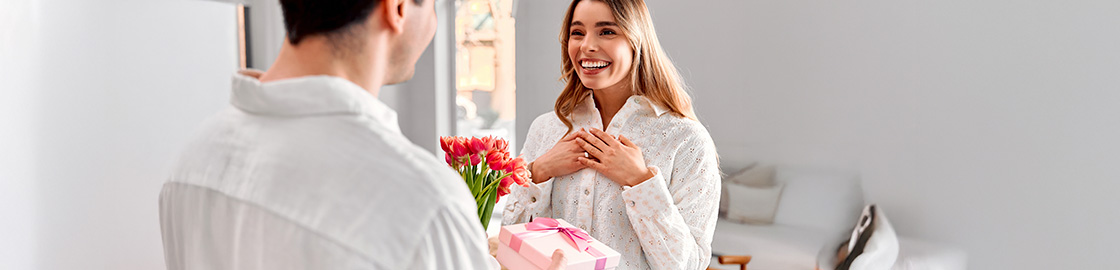 Foto de pareja en San Valentín donde un hombre le entrega flores y un regalo a una mujer.
