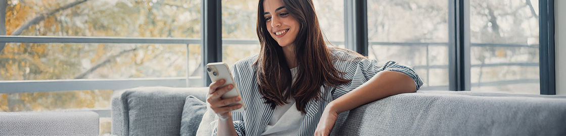 Foto de una muchacha sentada en un sillón, viendo apps en su smartphone mientras sonríe.