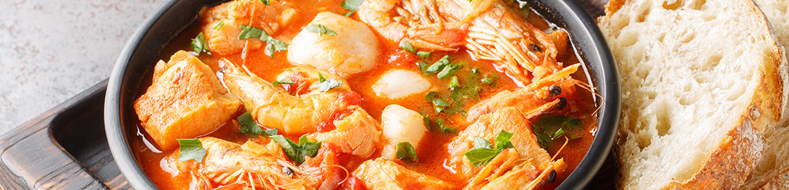 Foto de caldo de mariscos servido en un plato sobre tabla de madera, acompañado por rodajas de pan.