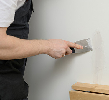 Foto de hombre terminando de resanar una pared con espátula flexible