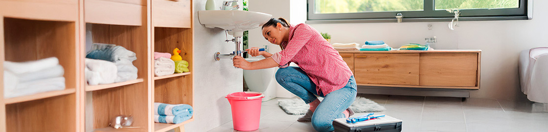 Foto de mujer reparando la tubería del lavabo del baño de su casa junto a su caja de herramientas