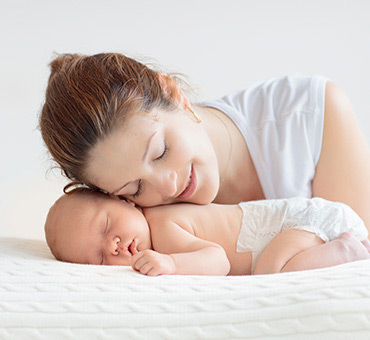 Foto de mujer posando su cara cariñosamente sobre su bebé dormido.