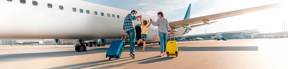 Foto de una familia (papá, mamá e hija) en la pista del aeropuerto, a punto de abordar un avión, con la niña saltando emocionada mientras toma de la mano a sus padres.