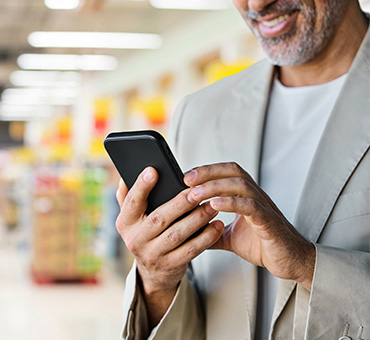 Foto de un señor sonriente viendo su celular mientras hace  sus compras en el súper. 
