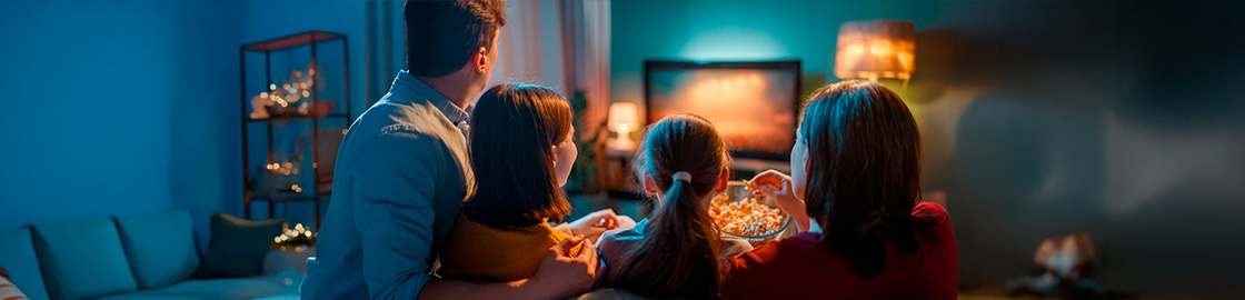 Foto de una familia feliz en la sala de su casa, viendo una película y comiendo palomitas de maíz.