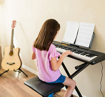 Foto de una niña en la sala de su casa tocando un piano eléctrico mientras lee la partitura.