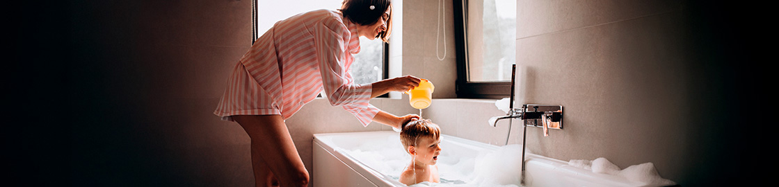 Foto de un niño en la tina mientras su mamá le enjuaga el cabello.
