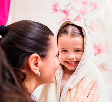 Foto de una mamá cubriendo a su hija sonriente con una toalla después de bañarse