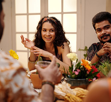 Foto de una joven mexicana sentada en la mesa durante la cena, con un joven al lado, conversando con el resto de la familia
