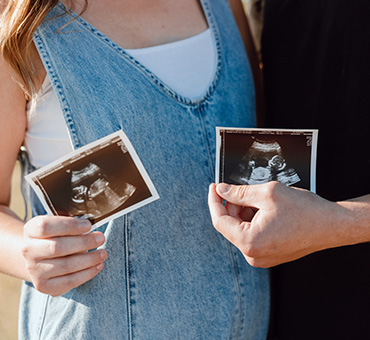 Foto de unos padres mostrando las fotos de un ultrasonido de sus dos bebés en gestación